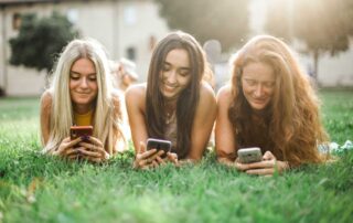 group of three teenage girls laying on the grass and looking at their cell phones